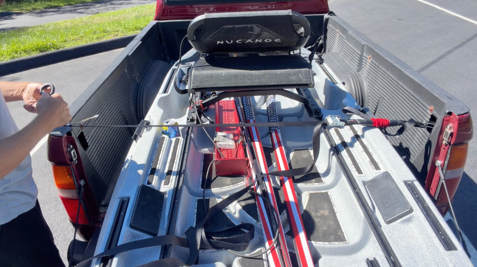 Daren positioning a TorkStrap across a fishing kayak in the bed of a red pickup truck.
