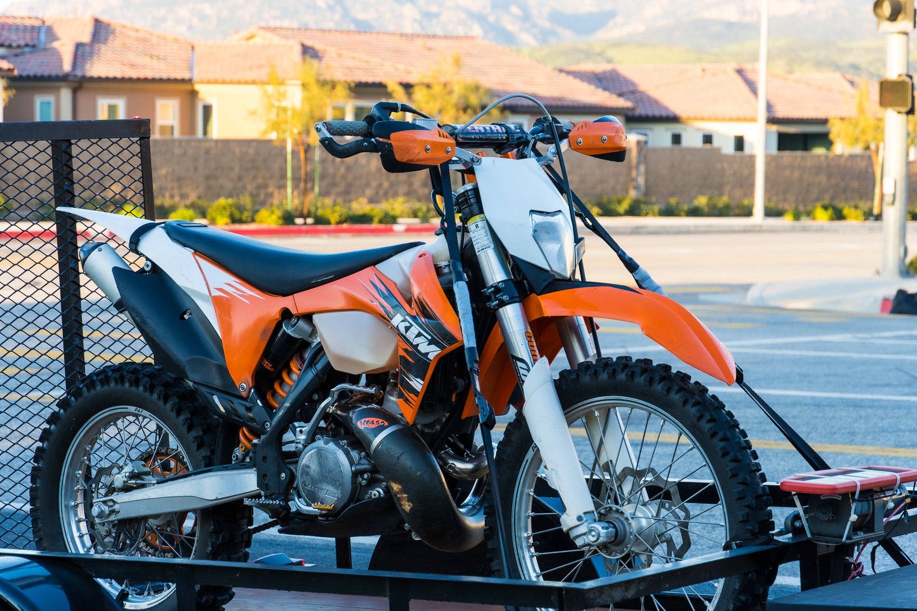 Dirt bike on utility trailer with spring-supported straps and soft-loop handlebar connections