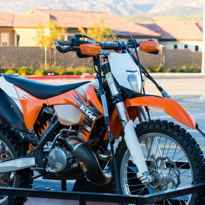 Dirt bike on utility trailer with spring-supported straps and soft-loop handlebar connections